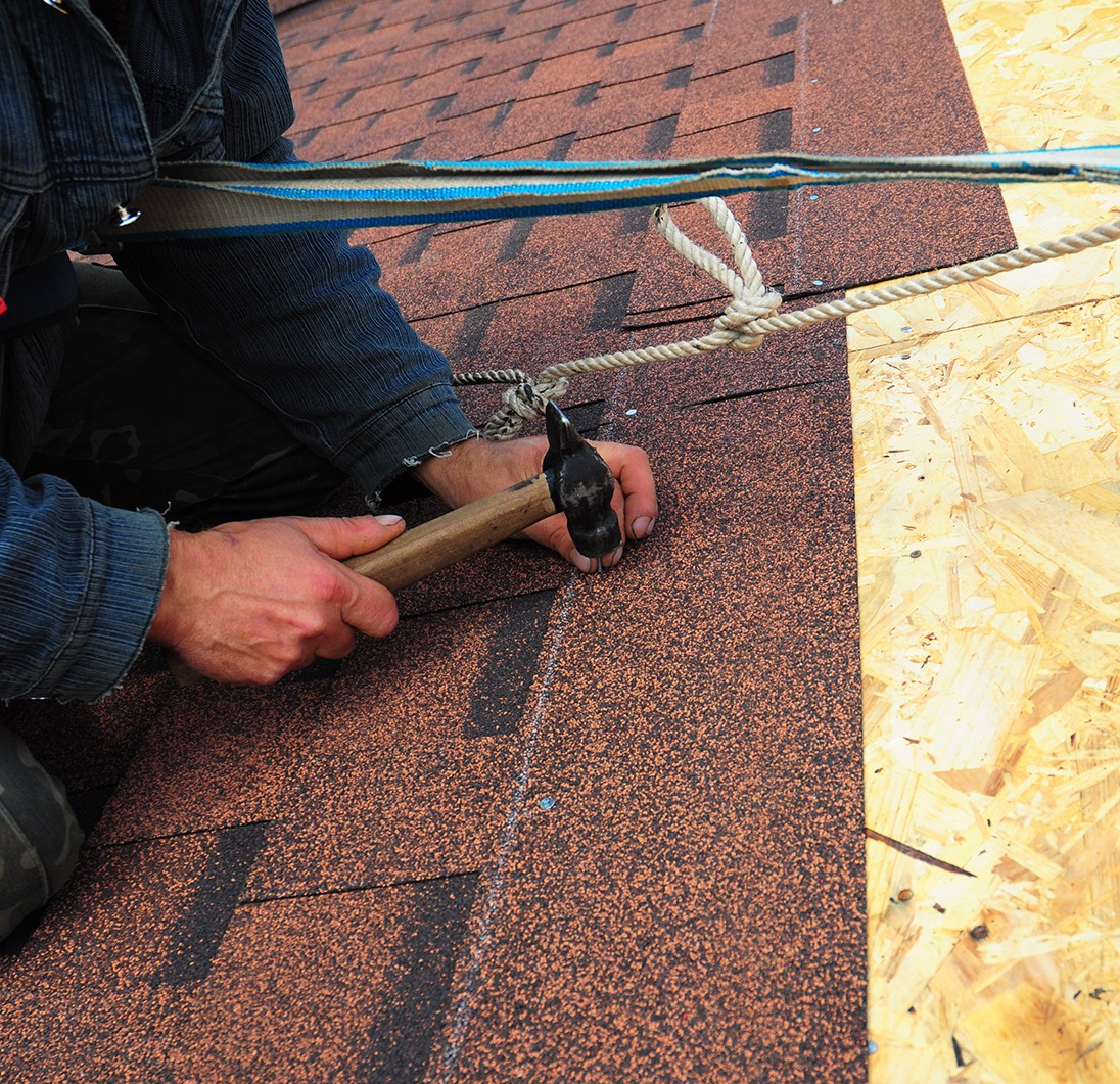 Worker installs bitumen roof shingles - closeup on hands