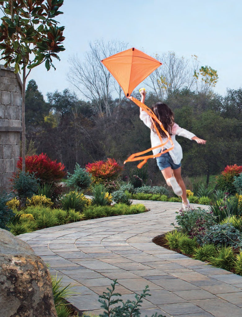 girl-with-kite-jumping-on-paved-walkway