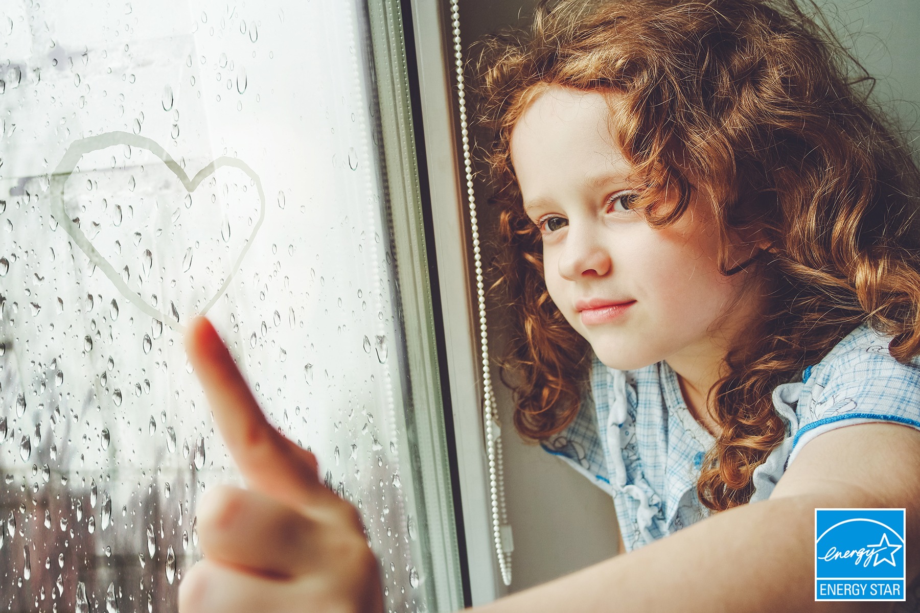 Happy child drawing heart on the window.